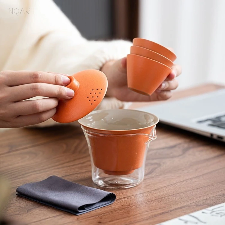The all-in-one tea set taken apart — the perforated lid held up in one hand, three cups stacked in the other, the bowl and the glass waiting below.