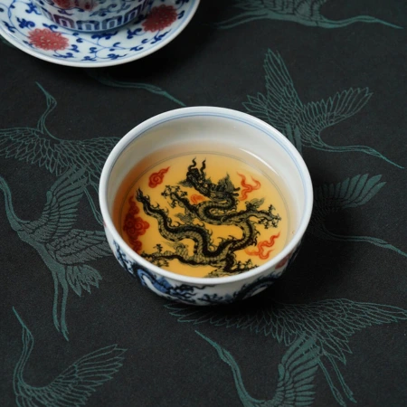 A hand-painted porcelain teacup filled with tea, its interior showing a dragon motif in dark blue and iron red