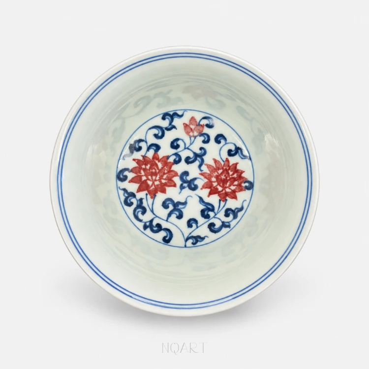 Inside the cup, a roundel of blue lotus scroll carries two red blooms, and the rest of the white glaze is left bare.