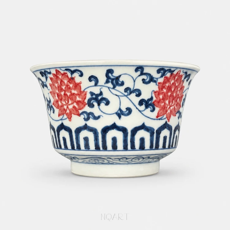 Two lotus blooms open across the wall of this Jingdezhen horse hoof cup, painted in underglaze red and joined by a cobalt vine that runs the whole way round.