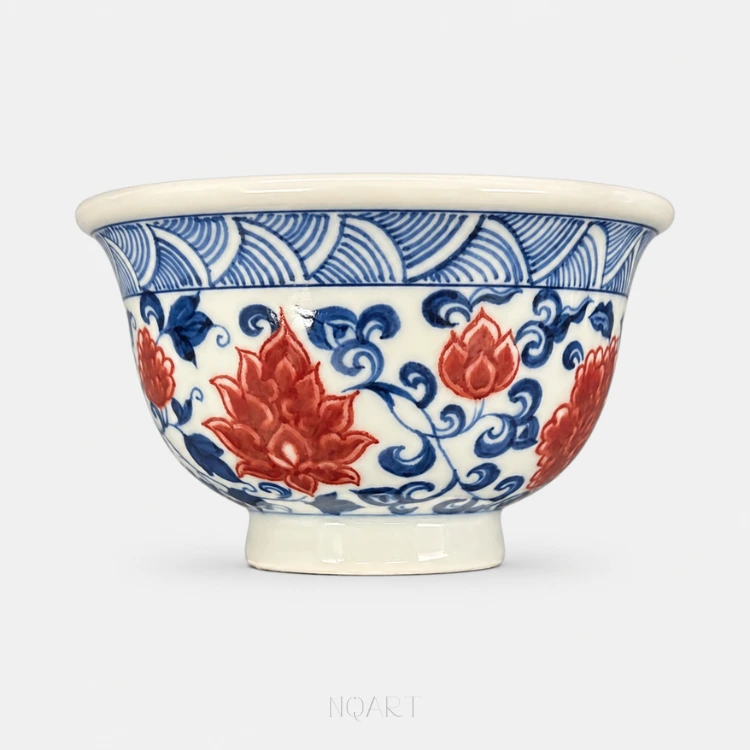 Under a band of pointed petals, the walls round out into a Ya Shou cup, painted with a lotus and chrysanthemum scroll in underglaze red and blue.