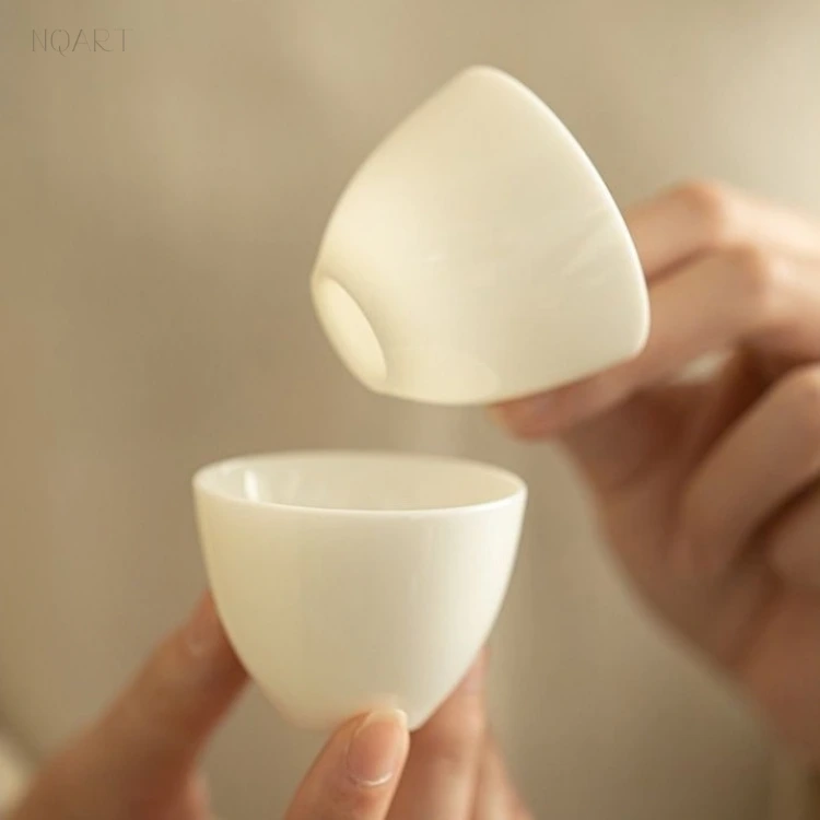 Two of the ceramic tea cups, one held upside down above the other, show how thin the wall runs — enough to make out the fingers behind.
