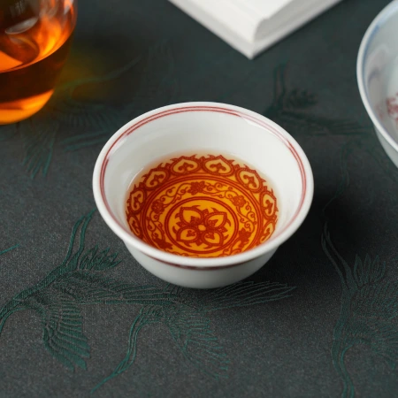 A porcelain teacup with an ornate gilt and iron-red medallion covering its interior, resting on a dark green cloth
