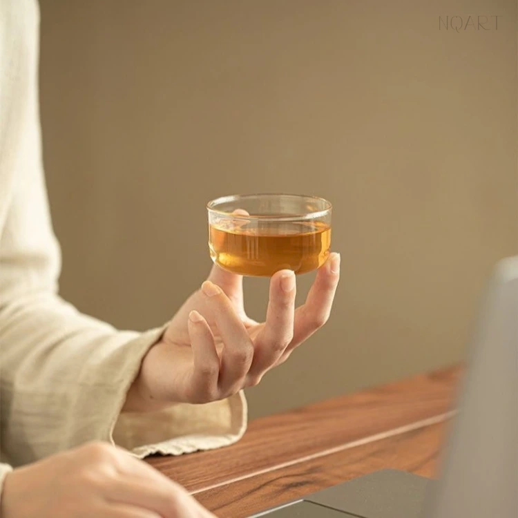 At the desk, the glass cup is wide and low — in a tea set for tea lovers, that is the shape that lets a hot pour spread and cool while the work goes on.