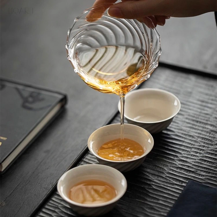 Tipped over the mat, the glass tea pitcher sends a thin stream down into one of the cups — the colour stays legible the whole way down.