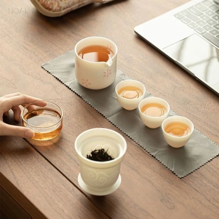 On the desk, the gongfu tea pitcher holds the pour while the strainer keeps the leaf, and one hand reaches across for the glass cup.