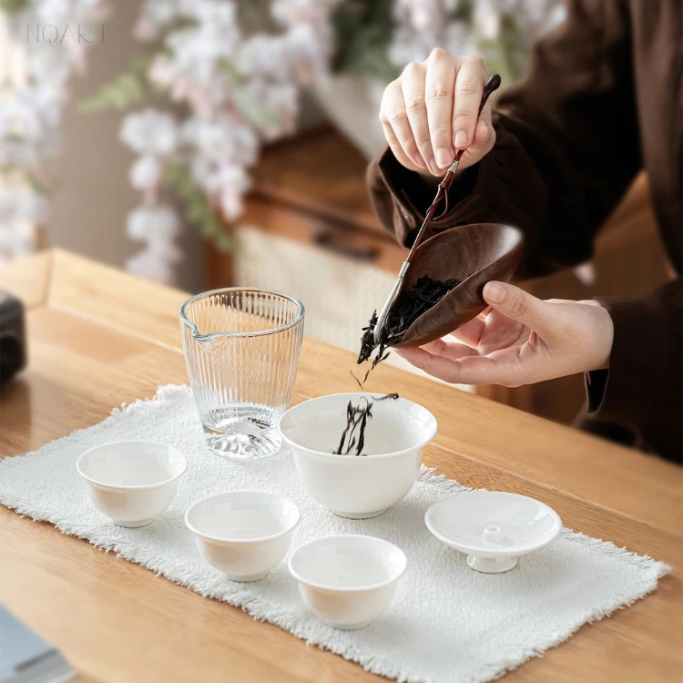 Loose leaf goes into the gaiwan of this compact gongfu tea set straight from a wooden scoop, the open lid set down beside the cups.