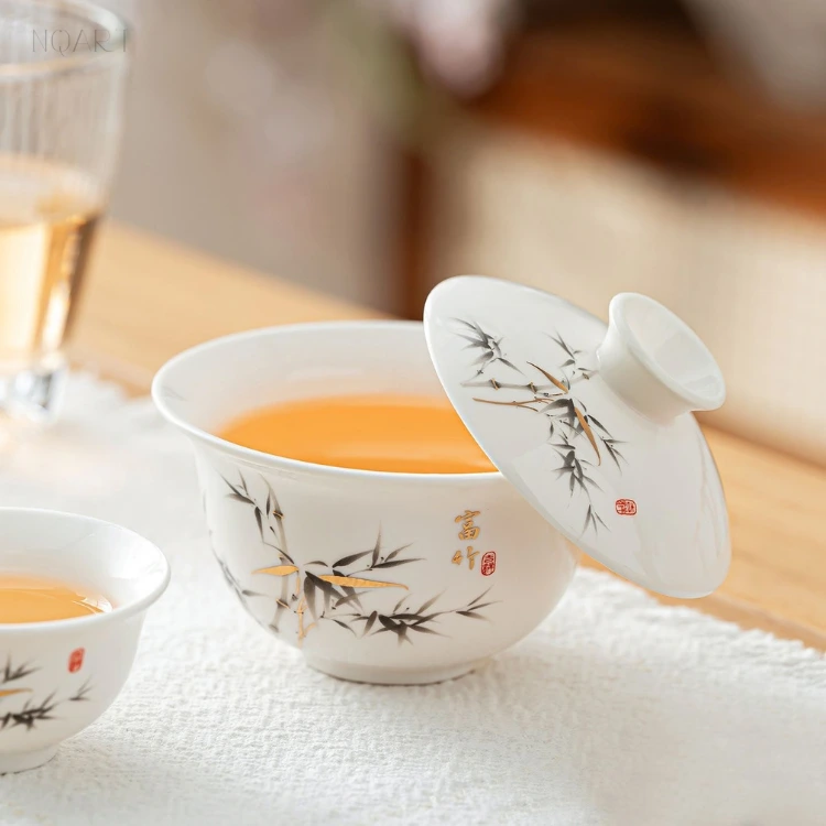 The porcelain gaiwan and its lid in the lucky bamboo pattern, the lid resting against the rim at an angle beside a gold inscription and a red seal.