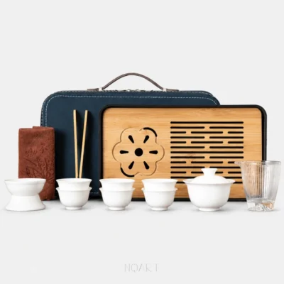 A ten-piece gongfu tea set with travel case on plain white — white porcelain gaiwan and cups, a faceted glass pitcher, a slatted tea tray, a tea towel and bamboo chopsticks, with the navy hard case behind them.