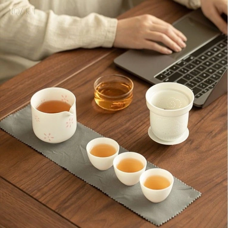 Beside a laptop, this office tea set sits on its cloth with the case unzipped behind — tea within reach without leaving the desk.