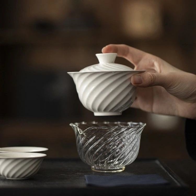 Hanging above the glass pitcher, the porcelain gaiwan shows both halves of this porcelain and glass tea set — the same fluting cut into opaque white and into clear glass.