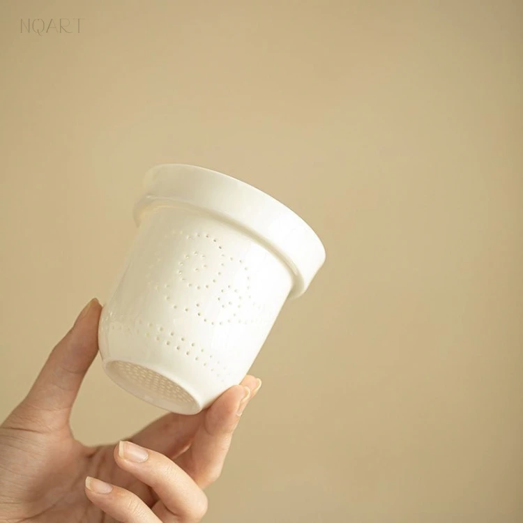 Up close on the porcelain strainer, the perforations are set in a pattern rather than drilled in rows — a flared lip, a rounded base, no handle.