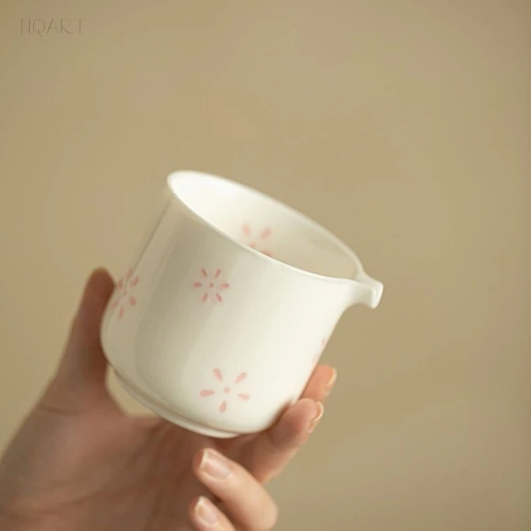 Turned in the hand, the brewing cup of this porcelain tea set carries a spout on one side and small pink blossoms scattered across the wall.