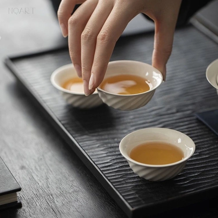 Off the mat and into the hand, one cup still full — a tea set for road trips divides every pour three ways, whichever two cups are left standing.