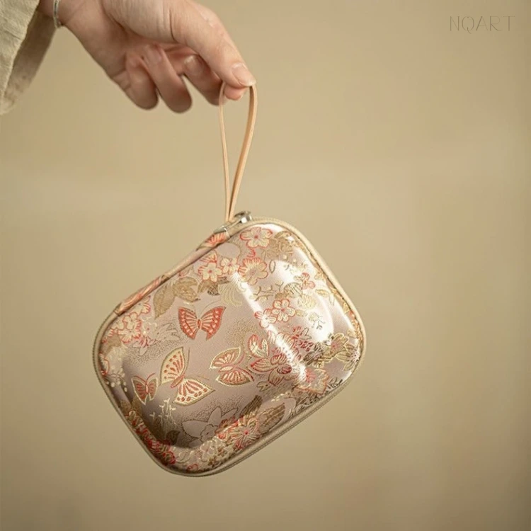 Held up by its strap, the tea set with storage bag swings clear of the table — floral print, gold zip and a hard shell that keeps its shape.