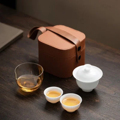 Against a dark table, this tea set with storage case sits closed among the pieces — glass pitcher, gaiwan and two cups, one larger than the other.