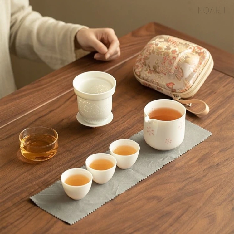 Set out on the wooden table, the tea strainer stands in its own small dish beside the brewing cup, with three cups of tea waiting on the cloth.