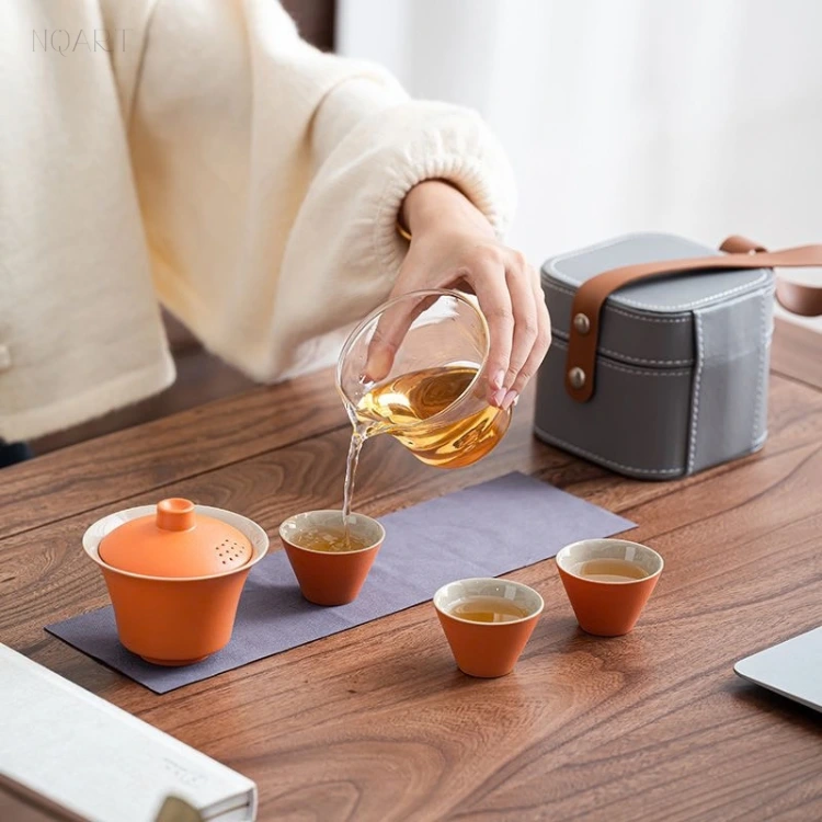 The glass pitcher tips tea into one of the three cups with the gaiwan resting behind it — the travel tea ceremony set partway through a session.