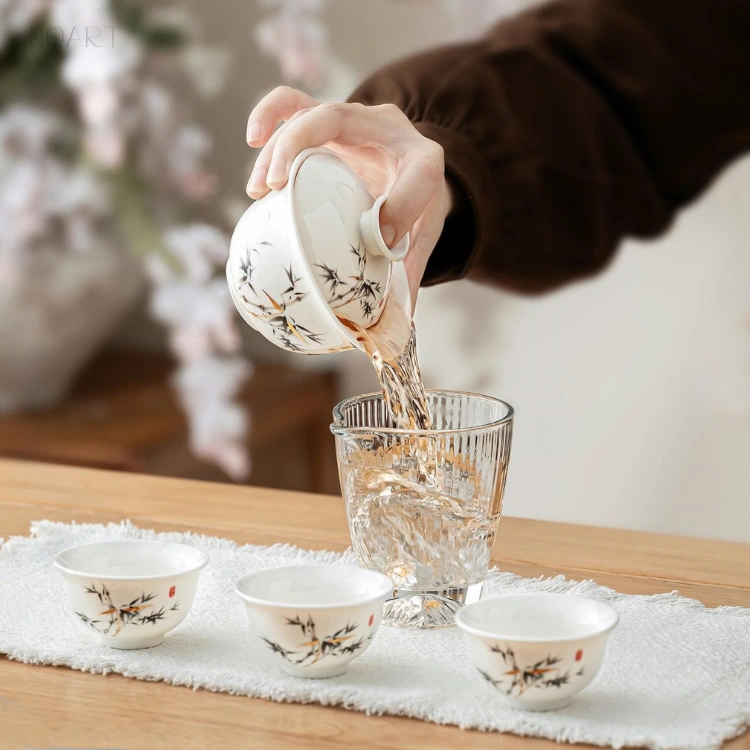 Pouring in the travel gongfu tea set — the porcelain gaiwan tipped with the lid held back between two fingers.