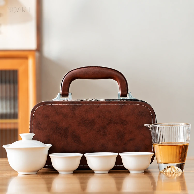 The travel tea set with carrying case unpacked on the table — six white porcelain pieces in front of the brown case that holds them.