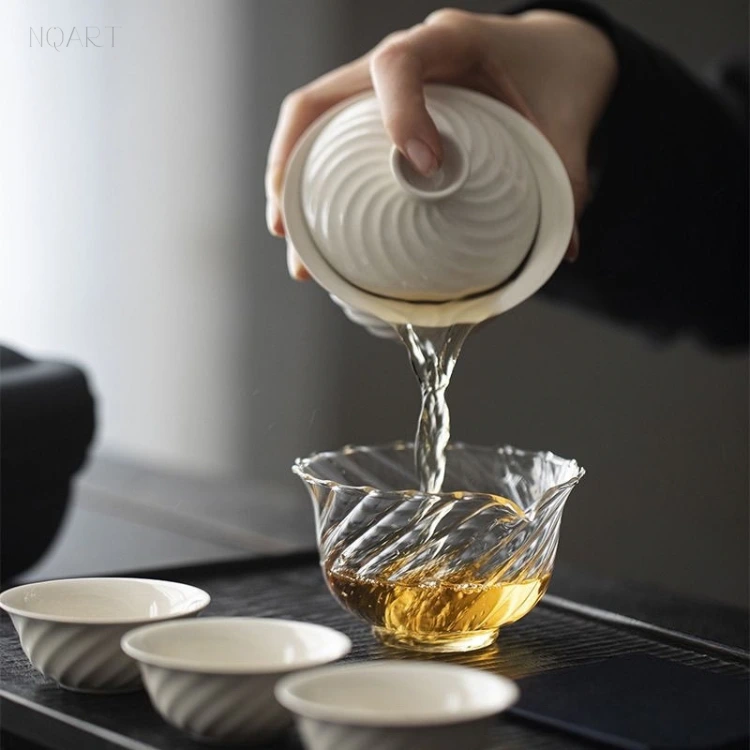 Held at an angle, the white porcelain gaiwan lets the tea out under the lid and down into the glass vessel below.
