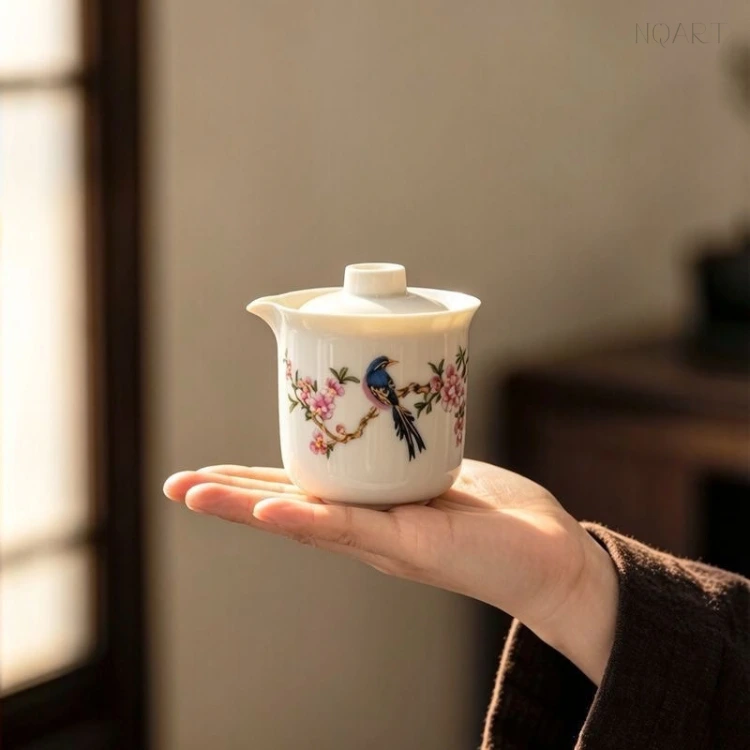 Backlit against a doorway, the bird and flower tea set shows its painting at full size — a blue-black bird on a flowering branch, with the spout on the left of the body.