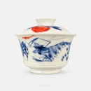 One blue crab holds the middle of this gaiwan, brushes of water plant around it and a small fish in underglaze red swimming past above.