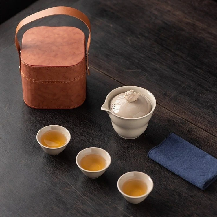 On the dark table, the bucket tea case stands with its arch handle up beside the bowl, the cups and the folded cloth.