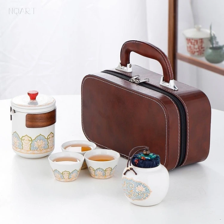 A five-piece tea set with its case standing open behind — brewing cup, three cups and the lidded jar arranged across a white table.