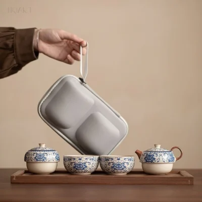 A four-piece tea set laid along a wooden tray — caddy, two cups and the pot — with the case lifted clear on its strap above them.