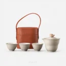 Everything the bucket holds, against white: a gaiwan tea set — the spouted bowl with its covered lid, three cups in a row, and the brown case standing behind them.