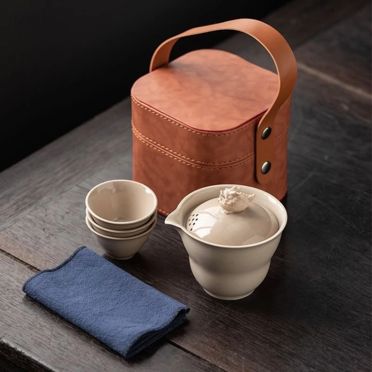 Beside the open case, the gaiwan with filter lid sits closed while the three cups nest inside one another on the cloth.