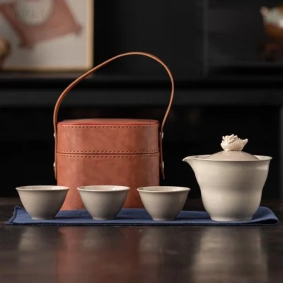Against the dark backdrop, this grey tea set sits on a blue cloth — case behind, three cups and the spouted bowl in front of it.