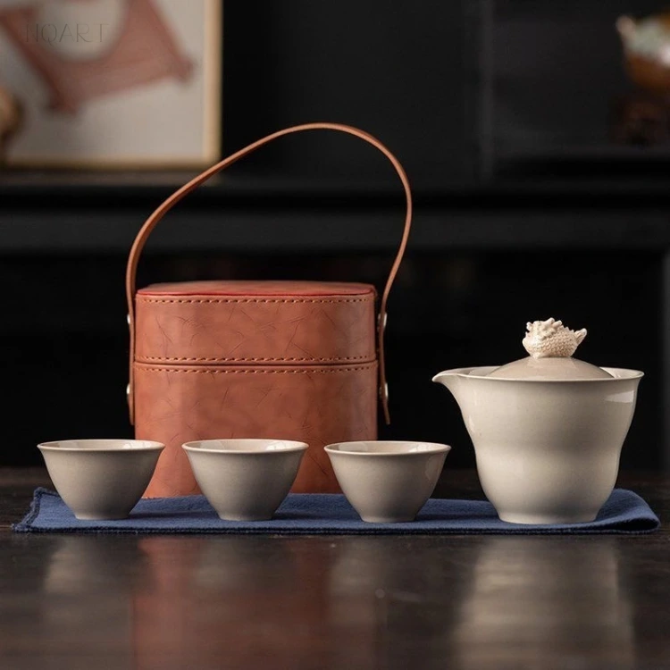 Against the dark backdrop, this grey tea set sits on a blue cloth — case behind, three cups and the spouted bowl in front of it.