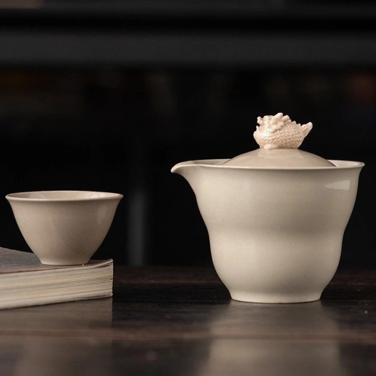 From the side, the porcelain gaiwan shows the lip of its spout and the step midway down the body, with one cup alongside.