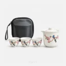 Four pieces and a case, on a white background: a portable tea set gift — a covered pitcher with a spout, three cups each painted with a bird on a flowering branch, and the black hard case standing behind them.