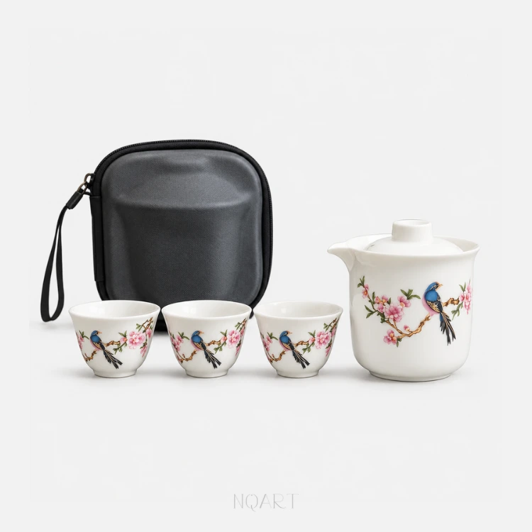 Four pieces and a case, on a white background: a portable tea set gift — a covered pitcher with a spout, three cups each painted with a bird on a flowering branch, and the black hard case standing behind them.