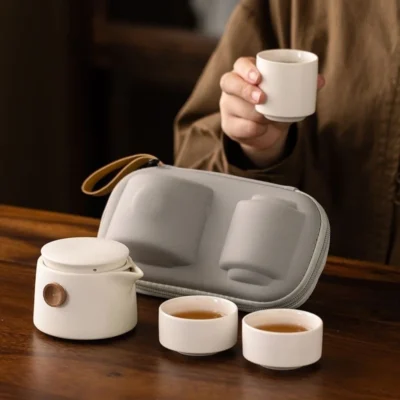 User pouring tea from the small ceramic teapot into cups, with the NQArt travel case in the background.