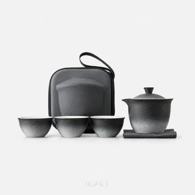Set straight on, against white: a spouted gaiwan tea set — the bowl with its pouring lip and pierced lid, three two-tone cups, and the black hard case standing behind them.