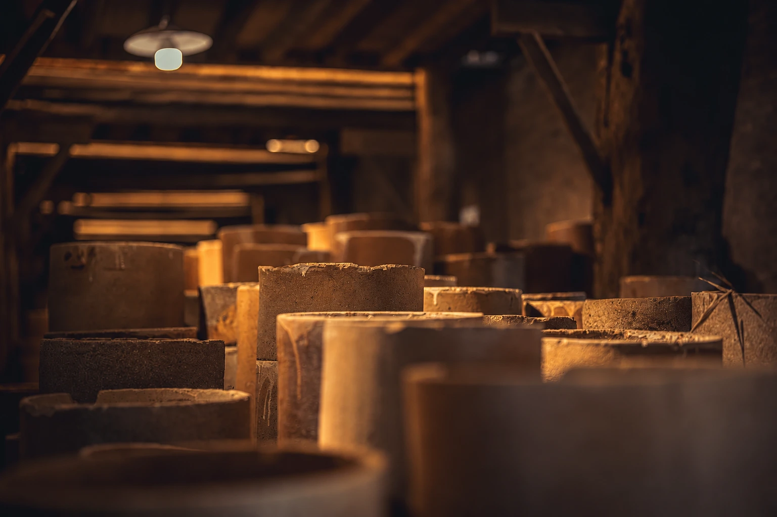 Stacked clay saggars lining a dimly lit kiln room, receding into shadow under a single hanging lamp