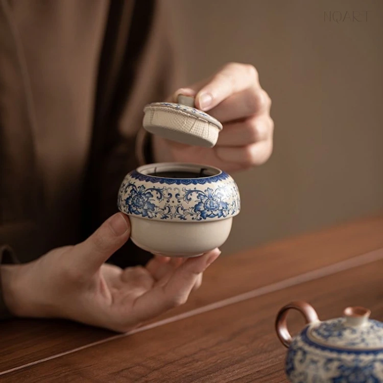 With the lid lifted away, the tea caddy shows the dry leaf sitting loose in the jar, the wooden knob still in the hand.