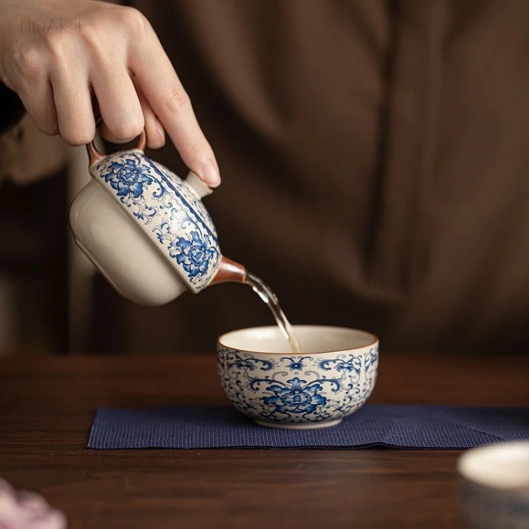 Over the cup, the wood handle tea pot pours through a short wooden spout, the blue-and-white scroll turning with it.